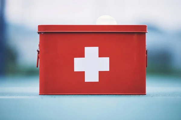 First aid, box and medical equipment for health emergency, response and treatment kit isolated in a blurred background. Red, cross and safety or medicine on a table for fast healthcare or cure.