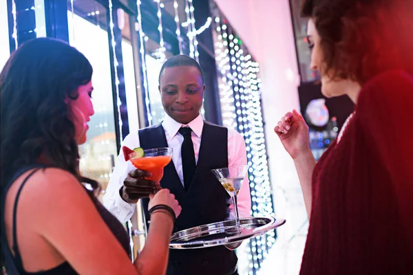 Cocktail for the lady...a waiter serving two women cocktails at a party