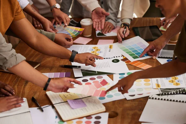 Creative, hands and color palette on table in meeting for planning, brainstorming or design strategy at office. Hand of group interior designers in teamwork, project plan or swatch ideas for startup.