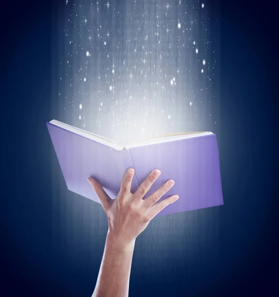 Stock image Shot of a hand holding an open storybook with light emanating from it.