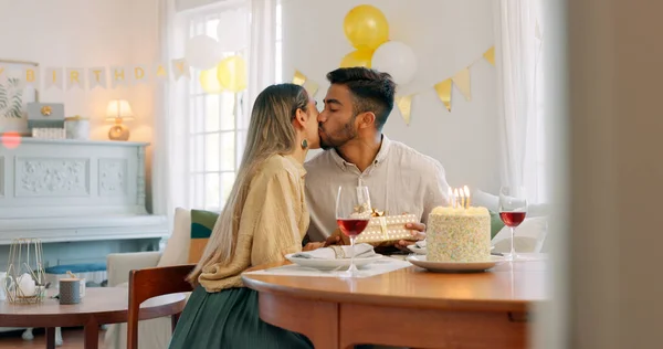 Couple, kiss and gift for birthday celebration, love and happy relationship together at home. Man and woman celebrating special day of birth in bonding happiness with cake and gifts at the table.