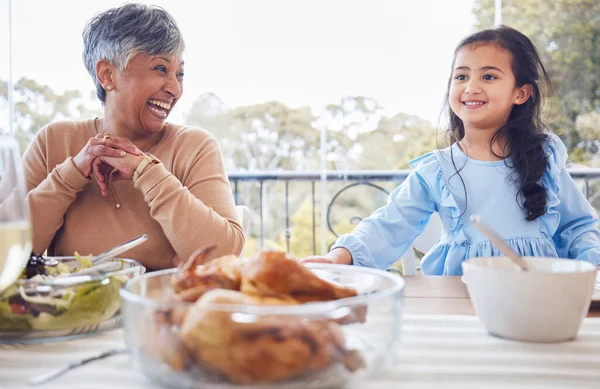 Family, food and grandmother with girl a table for lunch, part or social gathering on a patio. Love, dinner and senior woman laughing with grandchild while sharing a meal, happy and smile outdoors.
