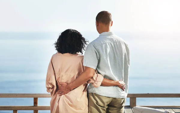 stock image Back, view and senior couple by beach, hug and enjoying quality time on holiday or vacation. Love, care and retired elderly man and woman hugging, embrace or cuddle while having fun by ocean or sea