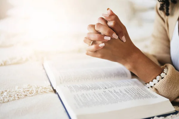 Prayer, bible and hands praying for religion, hope or help, spiritual or faith in home. God, christian and female or woman worship Jesus Christ or Holy Spirit with catholic text or book for peace