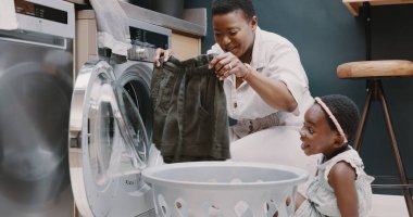 Çamaşır, anne ve çocuk bir evde birlikte kıyafet katlamaya yardım ediyorlar. Mutlu, heyecanlı ve genç bir kız, evinde çamaşır makinesinden giysileri temizlerken annesine yardım ediyor..