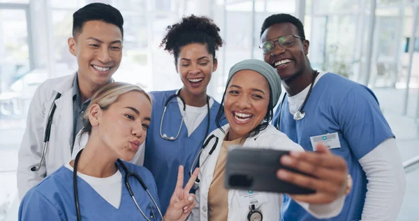 Doctors, team and selfie with diversity and health group, happiness with collaboration and smartphone photography. Medical professional, happy in picture and people in medicine with peace hand sign.