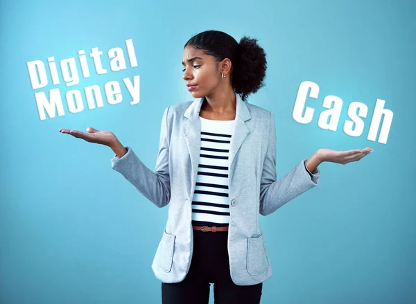 Studio shot of an attractive young woman weighing up her monetary options against a blue background.