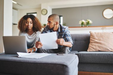 Stresli genç bir çiftin birlikte oturup finansal evraklarını incelerken çekilmiş bir fotoğrafı..