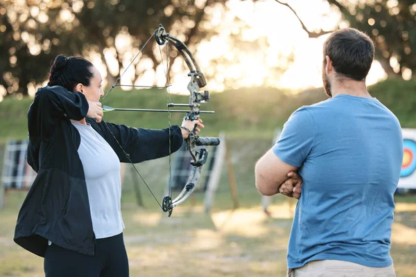 Archery, sports or help with a woman holding a bow and arrow outdoor for target practice with a coach. Coaching, learning or advice with a female and trainer at the shooting range for weapon training.