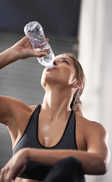 Sipping on some H2O to replenish her body. a young woman drinking from her water bottle at the gym