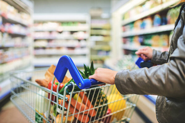 Cropped shot of a woman pushing a trolley while shopping at a grocery store.