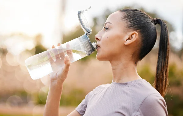 Fitness, health and woman drinking water in nature after exercise, training or workout. Sports, nutrition bottle and female athlete drink liquid for hydration after exercising, jog or cardio outdoors.