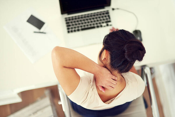 High angle shot of a young businesswoman holding her neck in discomfort while working at home.