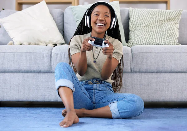 Black woman, gaming and smile with controller by living room sofa for fun match or online game at home. Happy African American female playing video games with headphones for entertainment or esports.