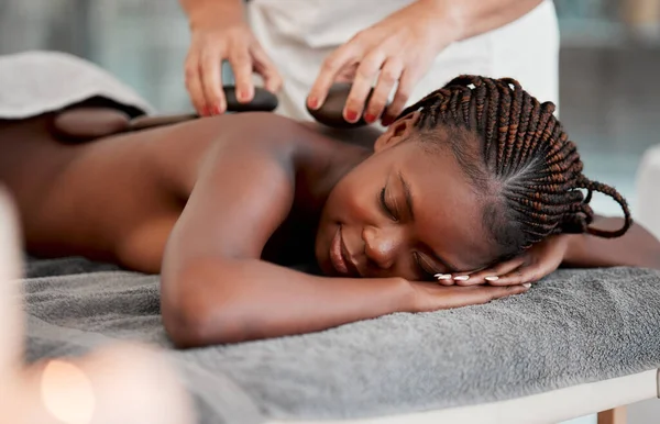 Black woman, hot stone massage and masseuse, hands and zen with holistic therapy and spa treatment. Calm, peace of mind and female, healing and stress relief with self care at wellness resort.