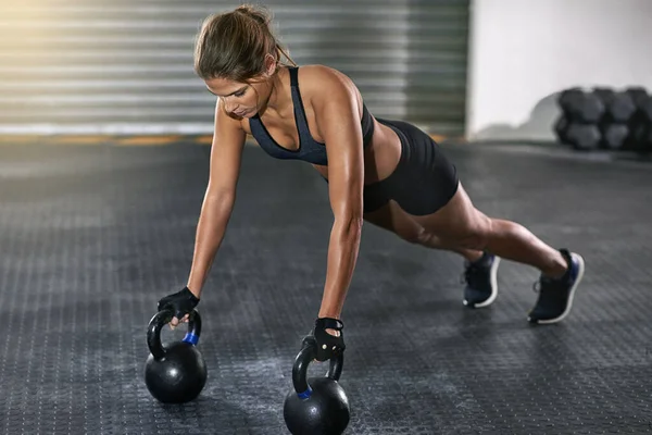 She trains like a beast. Full length shot of a young woman working out with kettle bells at the gym