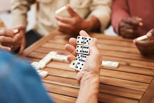 Hands, dominoes and friends in board games on wooden table for fun activity, social bonding or gathering. Hand of domino player holding rectangle number blocks playing with group for entertainment.