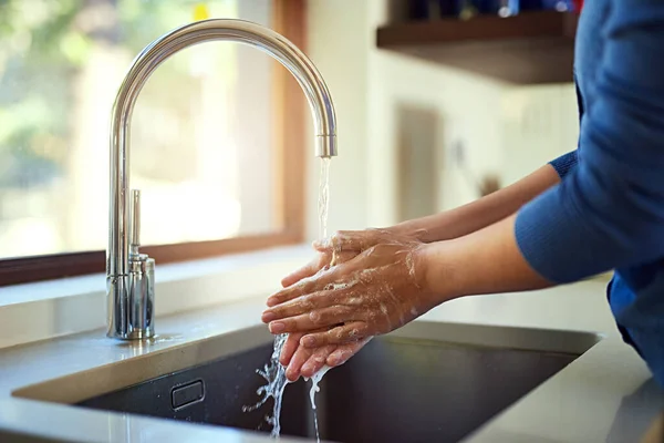 Shot of an unrecognizable woman washing her hands in the kitchen sink.