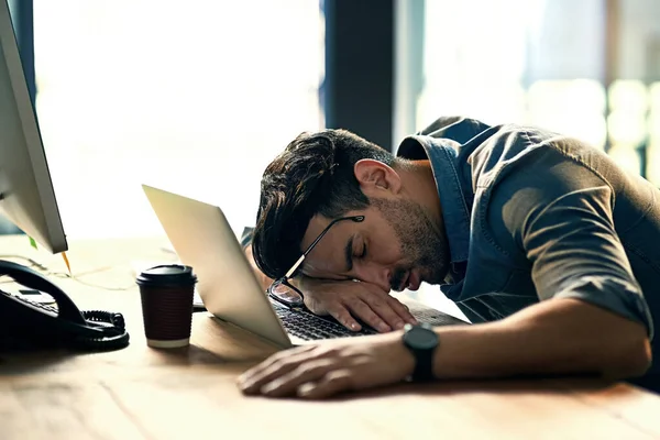 仕事の遅い夜の間に彼の机の上で眠っている疲れ若いビジネスマンのショット — ストック写真