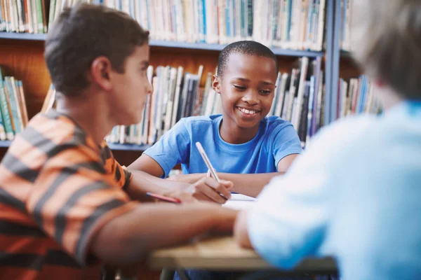 他喜欢写故事 一个非洲裔美国男孩坐在图书馆里和他的同学一起工作 — 图库照片