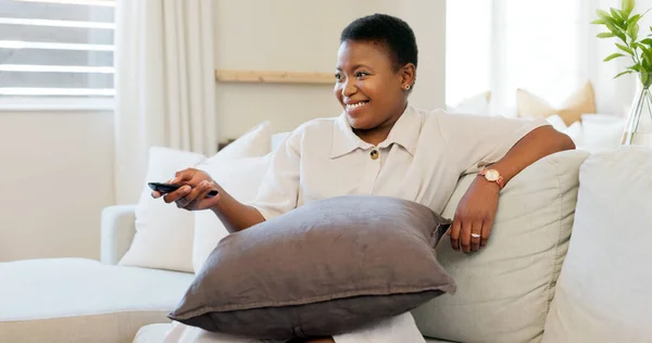 Happy, smile and black woman relaxing on a sofa while watching tv in the living room of her modern house. Happiness, laughing and African lady streaming a movie while sitting on a couch in her lounge.