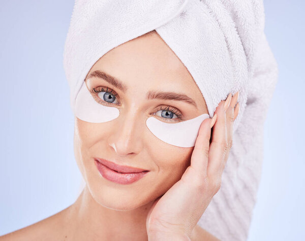 Skincare, face and woman with eye patches in studio isolated on a blue background. Dermatology portrait, beauty cosmetics and happy female model with towel and collagen facial mask for healthy skin