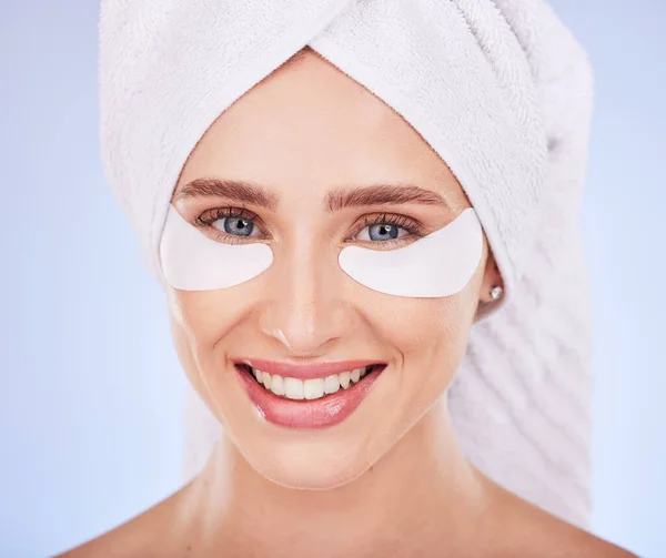 stock image Skincare, face and woman with eye patches in studio isolated on a blue background. Dermatology portrait, beauty cosmetics and happy female model with towel and collagen facial mask for healthy skin