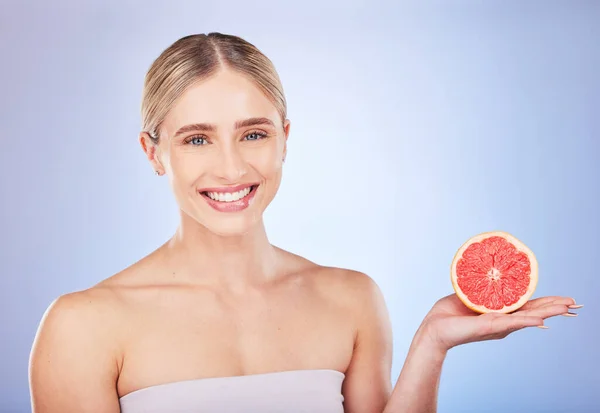 Skincare, face portrait and woman with grapefruit in studio isolated on a blue background. Food, fruit and happy female model with citrus for vitamin c, nutrition or diet, healthy skin or beauty