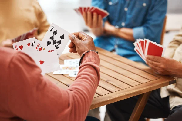 Senior friends, hands or playing card games on wooden table in fun activity, social bonding or gathering. Group of elderly men having fun with cards for poker game enjoying play time together at home.
