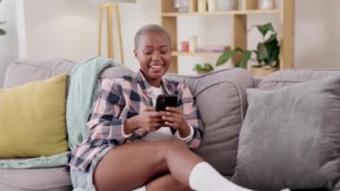 Gül, rahatla ve kanepeye yayılmış siyah bir kadınla telefonda konuş, sosyal medya ve komik mesajlar. Evde mesaj, tarama ve arama için bir kız oturma odasında kayan teknoloji, internet ve uygulama.