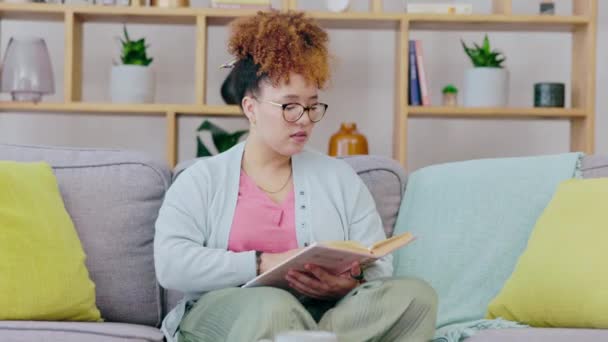 リビングルームのソファで読書やコーヒーをしている黒人女性は 自宅でリラックスして落ち着いています 朝は本や大学の教科書と一緒に休むソファの上で若い人のラウンジ 本を読む — ストック動画