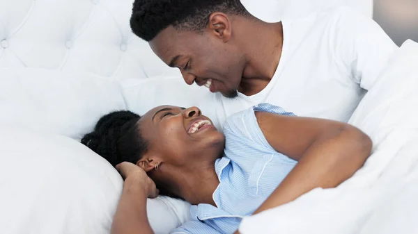 Happy black couple in bedroom kiss and smile for love, romance and intimacy at house or home in morning. Young, happiness and kissing black woman and man or romantic black people dating bond together.