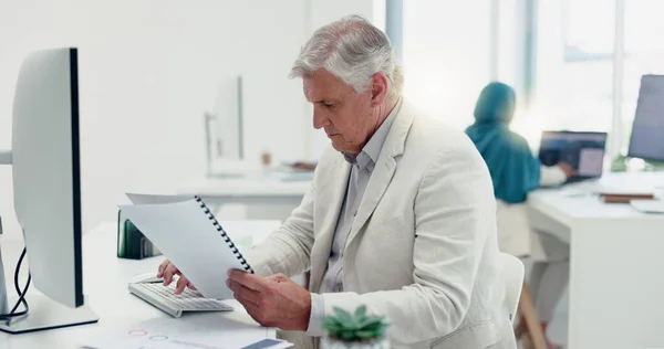 Business man, computer and documents while working in a office for data analysis while typing online doing research. Senior entrepreneur at his desk with a file for information on a finance report.