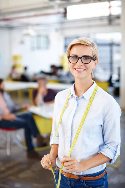 The measure of success. Portrait of a young woman standing with a tape measure around her neck and colleagues colleagues in the background