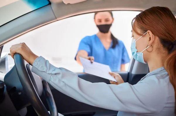 車の中でCovidテストと運転中 看護師は記入する患者のフォームを与えます 車の中でマスクを着用し 医療従事者からの文書を取る女性 マスク コロナウイルスおよび遠隔地でのテスト — ストック写真