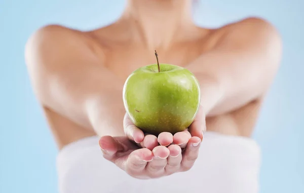 Hands of woman, holding out healthy apple or health, wellness and food on a blue background. Beauty, care and nutrition of model or girl with ripe, juicy fruit and vitamins for a lifestyle diet