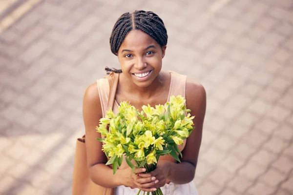 Flowers, gift and black woman with smile for bouquet for birthday or celebration in the street from above. Face of an African girl with a present of yellow lilies in the road and the city of France.