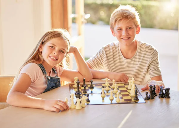 Portrait, chess and children relax at a table with board game, bond and learning in a living room in their home. Kids, chessboard and brain activity by girl and boy playing, planning and thinking.