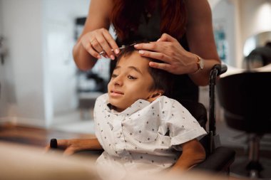 Kuaför, sakatlık ve tekerlekli sandalye özürlü çocuk. Serebral felçli, kuaför saçlarını kestiriyor. Meksika 'da kuaför kadının makasıyla profesyonel saç tıraşı olan genç bir çocuk.