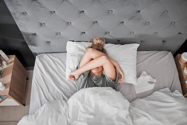 Tired, sad and sick woman in bed with insomnia in the bedroom of house from above. Top view of girl with depression, anxiety and mental health problem thinking of sleep, stress and burnout in home.