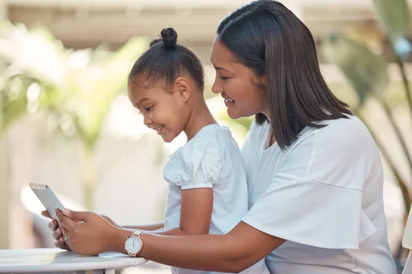 Mother, girl and tablet streaming cartoon, video or education game for children while sitting outdoor. Latin woman and her young daughter watching funny children movie online with technology.