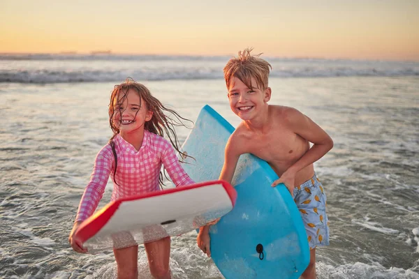 Happy children, beach and learning to surf for fun and bonding on bali summer vacation. Kids, boy and girl siblings on tropical holiday while surfing with board for water sports, splash and swim.