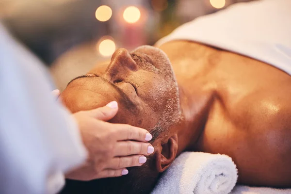 Hands, old man and head massage at spa for wellness, relax and health. Bokeh, peace and zen with elderly male on massage table with masseuse for stress relief, facial treatment or physical therapy