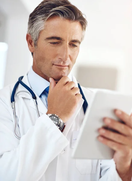 我想知道 一个英俊而成熟的男医生站在医院走廊里拿着一个数码平板电脑 — 图库照片
