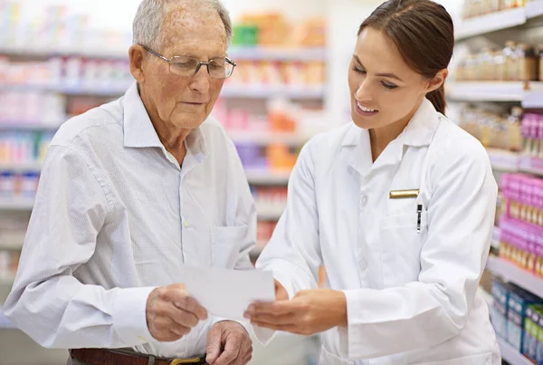 Ensuring her client is well informed. a young pharmacist helping an elderly customer with his prescription