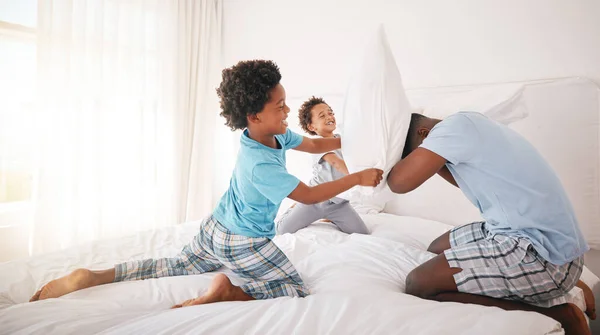 Black family, pillow fight and bedroom bonding of a father, children and fun in a home. Papa, kids and crazy play fighting of youth with energy in the morning in a house with dad feeling love.