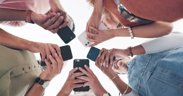 Hands, phone and communication with friends standing in a huddle or circle from below for networking. Social media, mobile and 5g with a man and woman friend group connected to the internet together.