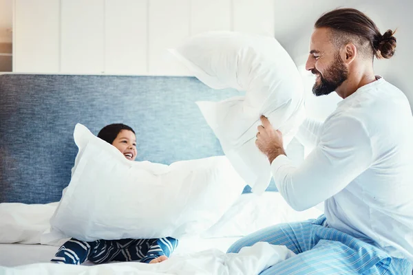 Happy, love and father in pillow fight with his child on the bed in the bedroom of family house. Happiness, smile and dad being playful with his boy kid while bonding, playing and having fun at home