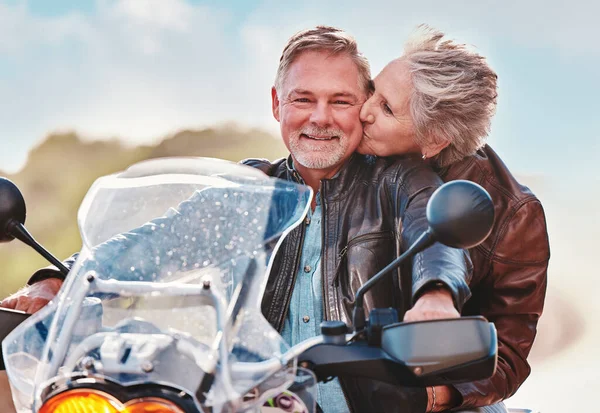 Travel, kiss and senior couple on motorcycle for adventure, freedom and road trip on weekend in retirement. Love, travelling and happy man and woman ride on motorbike for holiday, vacation or journey.