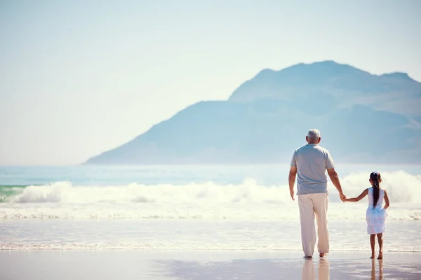 stock image Holding hands, relax and grandfather with child at beach for holiday, bonding and vacation mockup. Affectionate, travel and happiness with old man and girl walking for summer break, fun and support.